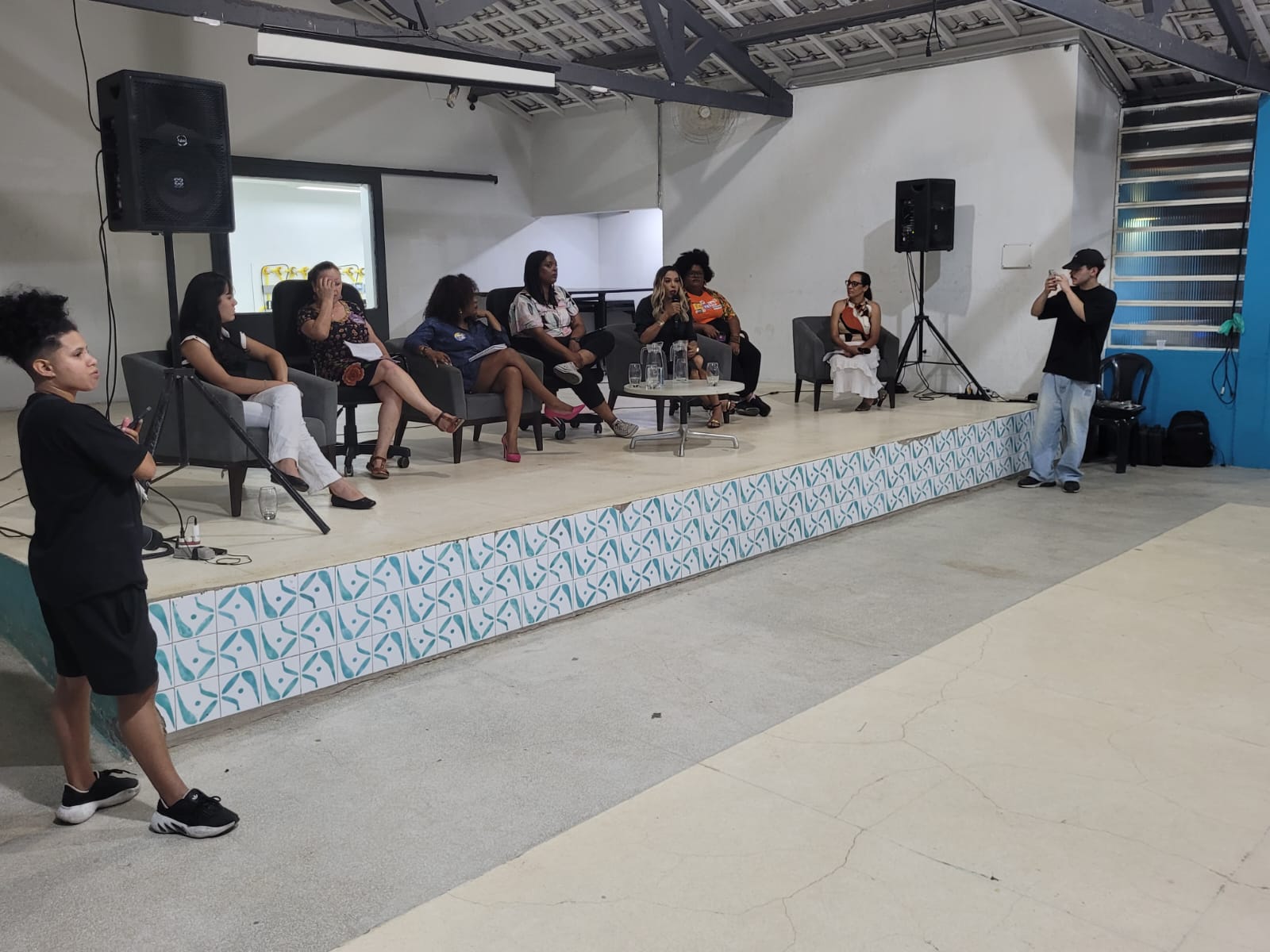 Imagem do palco do Galpão ZL, no qual estão sete pessoas. A foto ilustra o texto sobre o evento 2º Encontro Mulheres na Política: conversa com candidatas a vereadoras.