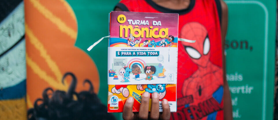 Imagem de uma criança segurando um gibi da 'Turma da Mônica' durante distribuição de kits referentes ao projeto 'Contar Histórias na Primeira Infância é Para a Vida Toda',