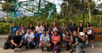 Imagem da comitiva do Jardim Lapena durante a visita a Medellín, na Colômbia. O grupo está à frente de uma área arborizada e de uma estrutura metálica disponível na cidade.