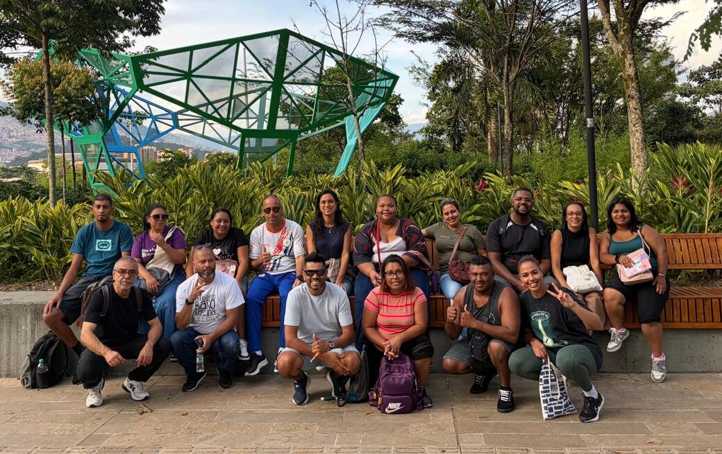 Imagem da comitiva do Jardim Lapena durante a visita a Medellín, na Colômbia. O grupo está à frente de uma área arborizada e de uma estrutura metálica disponível na cidade.