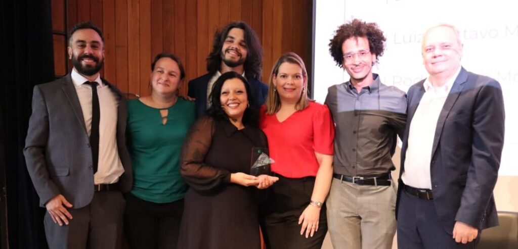 Foto da equipe da Secretaria Municipal de Saúde. Há seis pessoas da equipe no palco (três homens e três mulheres). Elas e eles estão com Armando Luis Palmieri, secretário-executivo de Gestão Administrativa da Secretaria Municipal da Saúde.