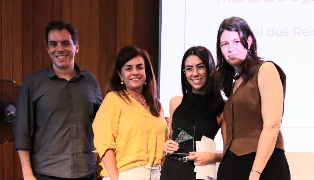 Equipe da Secretaria Municipal de Mobilidade Urbana e Transporte. Há um homem e duas mulheres no palco. Elas e ele estão com Mariana Almeida, diretora-executiva da Fundação Tide Setubal.