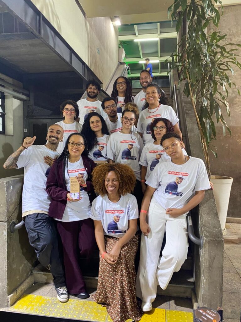 Há 13 pessoas em uma escada. Uma das que estão à frente segura o troféu do Prêmio MOL de Jornalismo pela Solidariedade. Todas elas usam camisetas com uma foto e informações sobre Helber Alves.