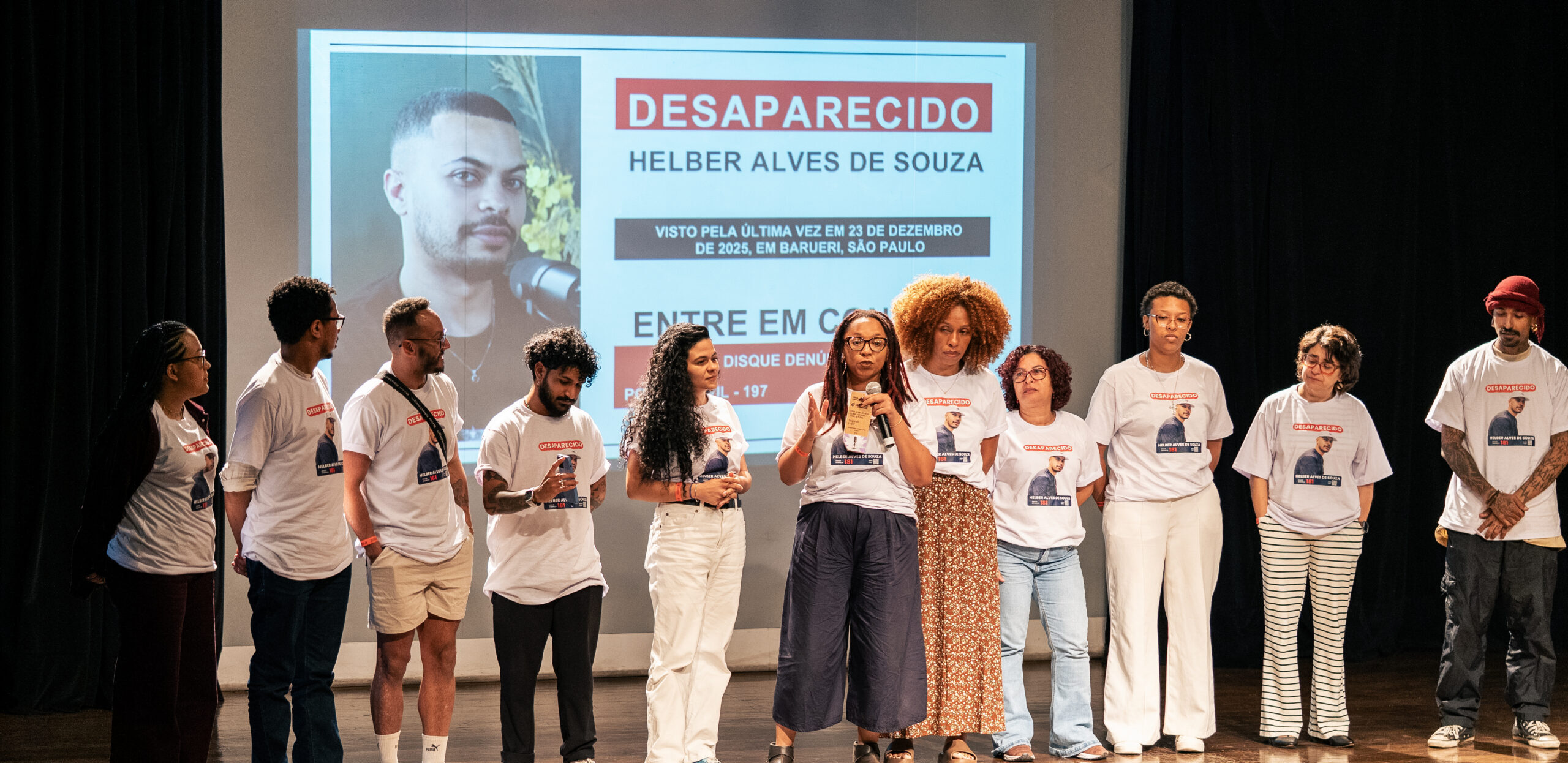 Imagem de integrantes da Fundação Tide Setubal e de Geledés - Instituto da Mulher Negra durante a entrega do troféu de segundo lugar no 4° Prêmio MOL de Jornalismo para a Solidariedade. Todas as pessoas estão com camisetas com a foto de Helber Alves, coapresentador do podcast 'Essa Geração pelo Clima', que está desaparecido desde 24 de dezembro de 2025.