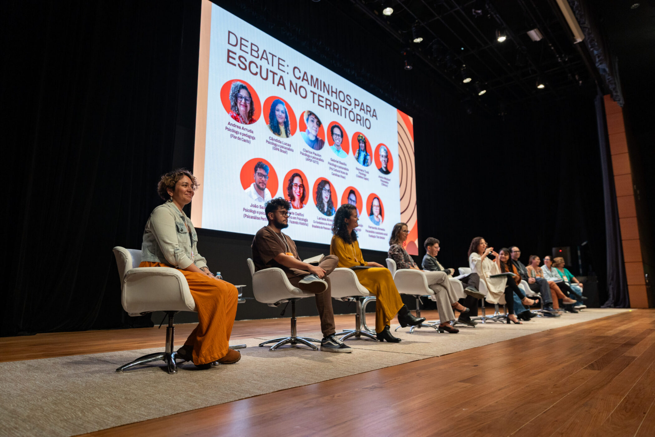 Imagem do palco com as pessoas participantes da segunda mesa do Seminário Territórios Clínicos - Segunda Edição. Elas estão no palco e à frente de uma tela projetada com as fotos delas.