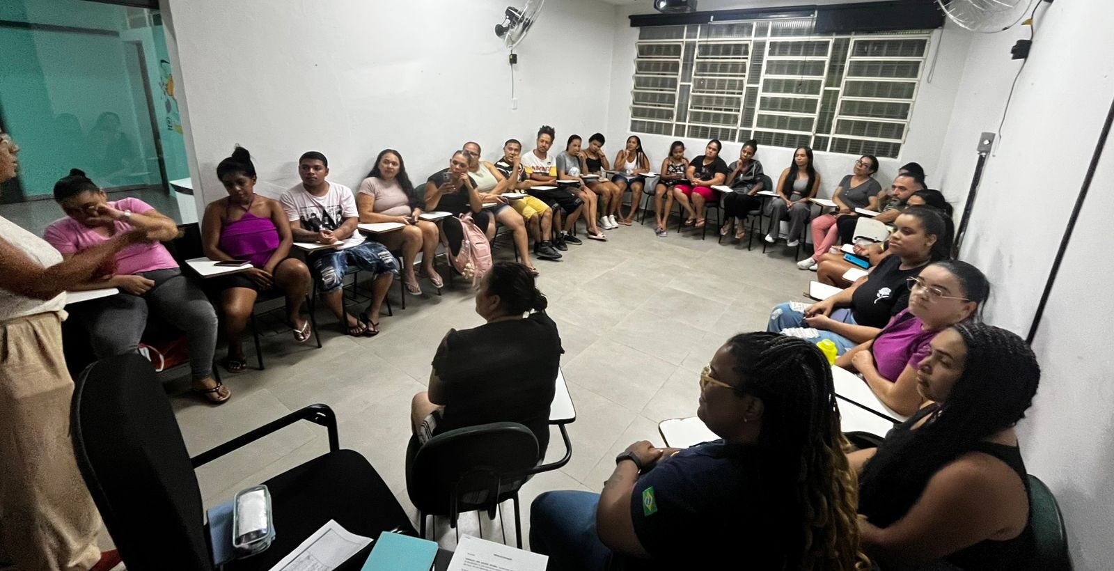 Imagem de reunião do Projeto Asas + Espaço Jovem em uma das salas do Galpão ZL. Há, naquele espaço, adolescentes sentadas e sentados em cadeiras dispostas em formato de "U" ao redor do ambiente.