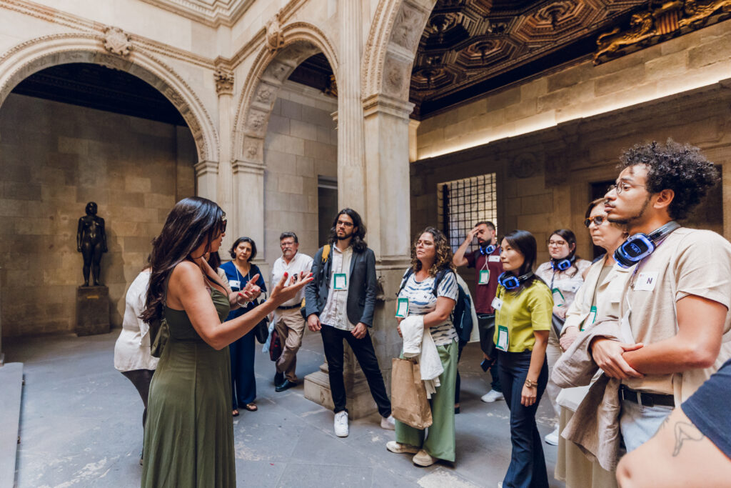 A imagem mostra a comitiva que participou do intercâmbio em Barcelona durante uma visita guiada. O grupo aparece em momento no qual recebe informações de representante do poder público local.