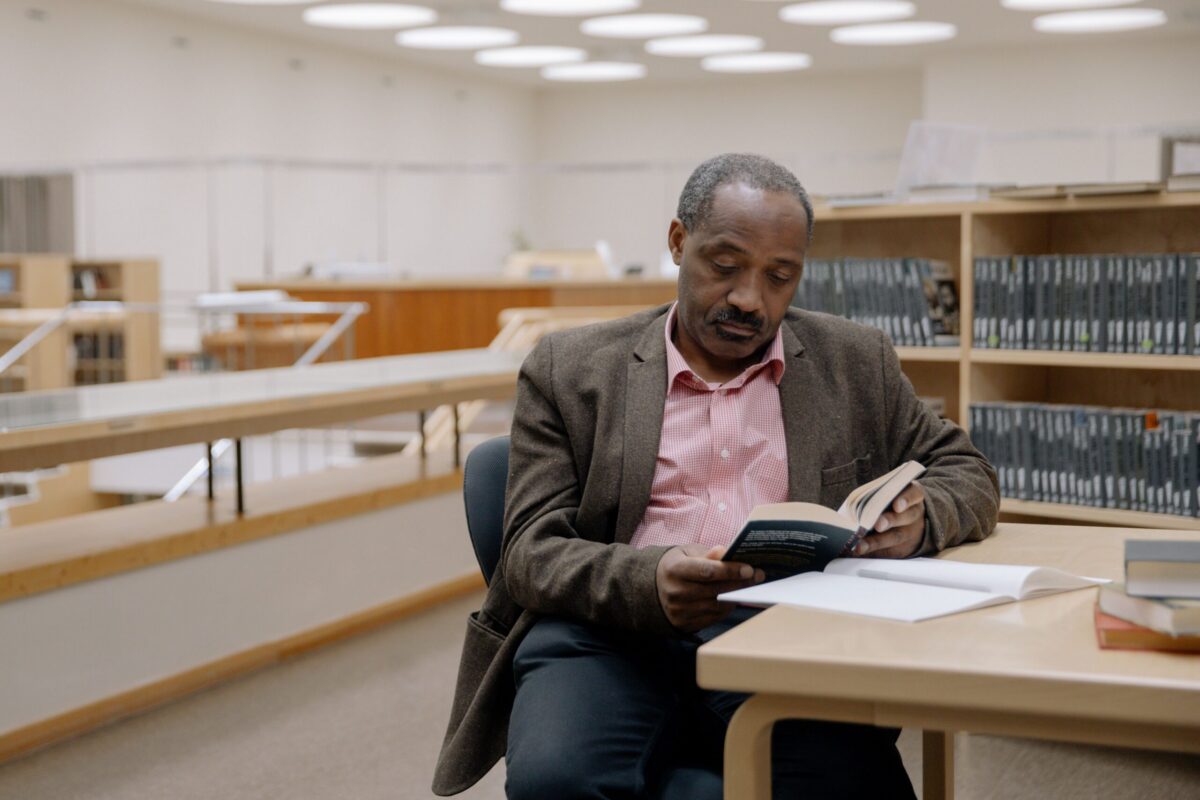 Imagem de um homem lendo um livro em uma biblioteca. A foto ilustra a lista de cinco livros sobre tópicos para combater desigualdades na saúde mental.