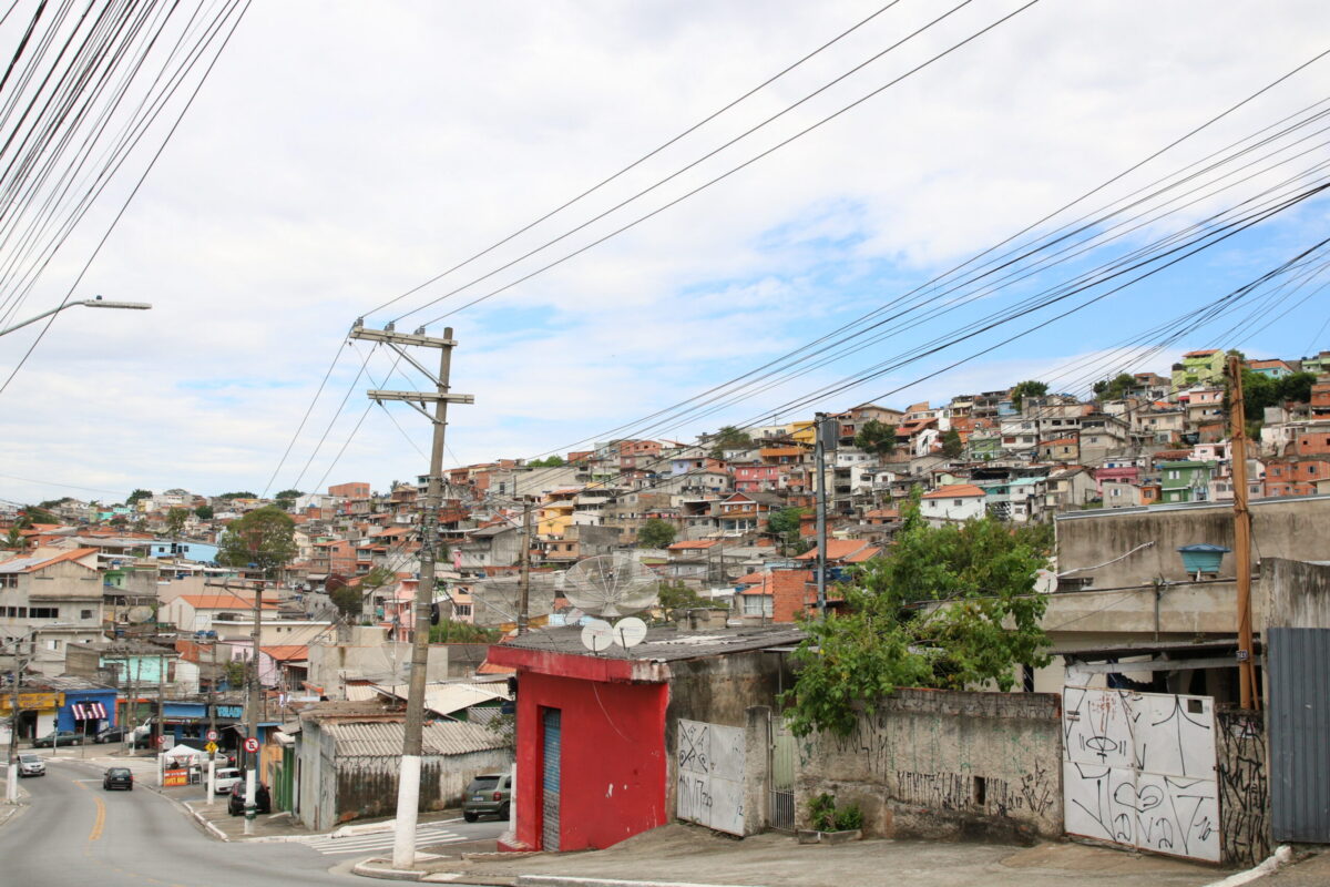 Imagem da vista de Perus, em São Paulo. É possível ver, à esquerda, uma avenida que corta a região. Aparecem à direita diversas casas de alvenaria que compõem o horizonte, assim como postes com fiação elétrica.