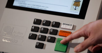A imagem mostra uma urna eletrônica e um dedo pressionando a tela "Confirma" (na cor verde). A foto ilustra a nota sobre o Filtro Periférico da Fundação Tide Setubal.