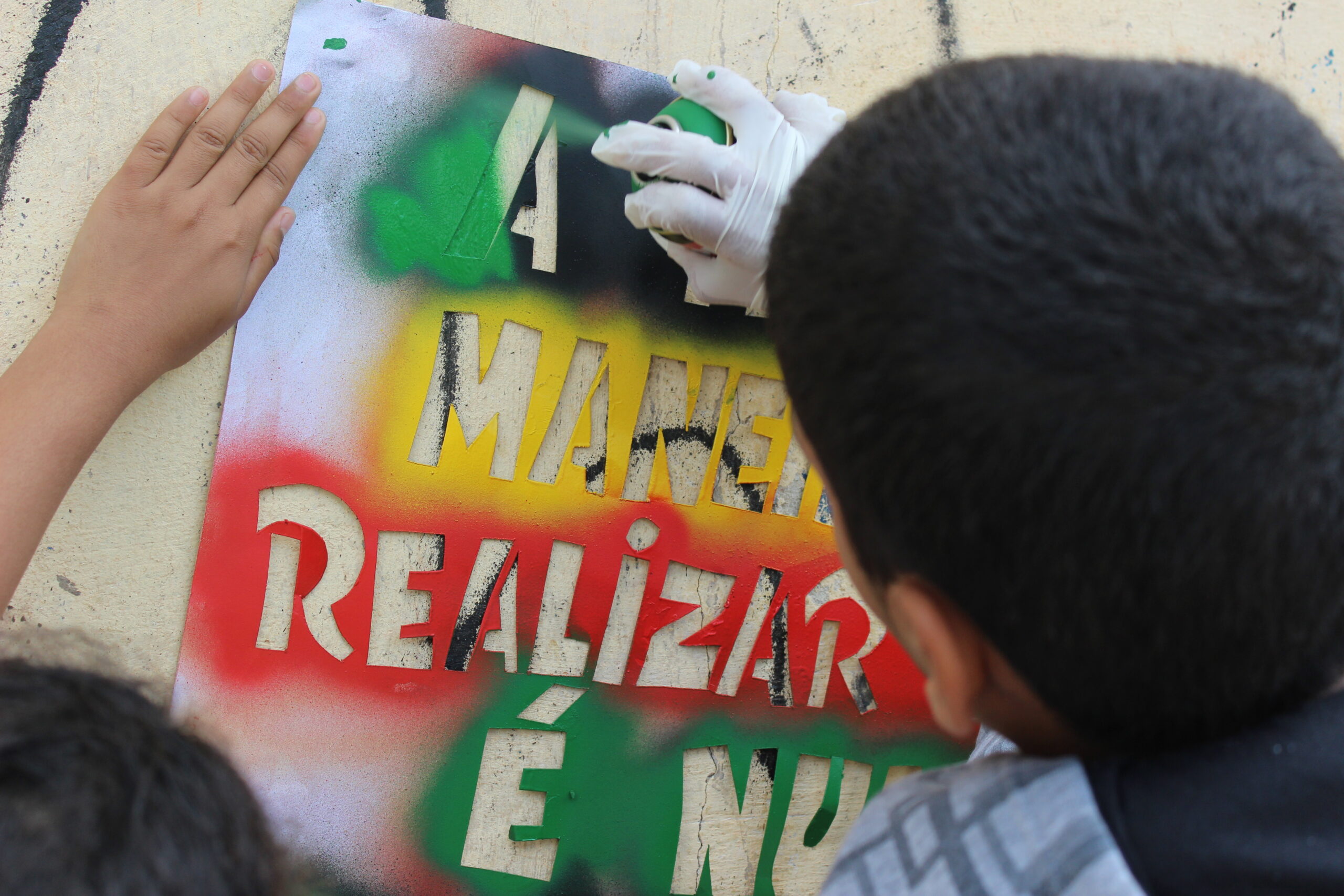 A imagem mostra uma pessoa fazendo uma pintura com stencil com as cores verde, amarelo e vermelho. A foto ilustra o manifesto da Fundação Tide Setubal sobre a importância de colocar o território no centro das eleições.